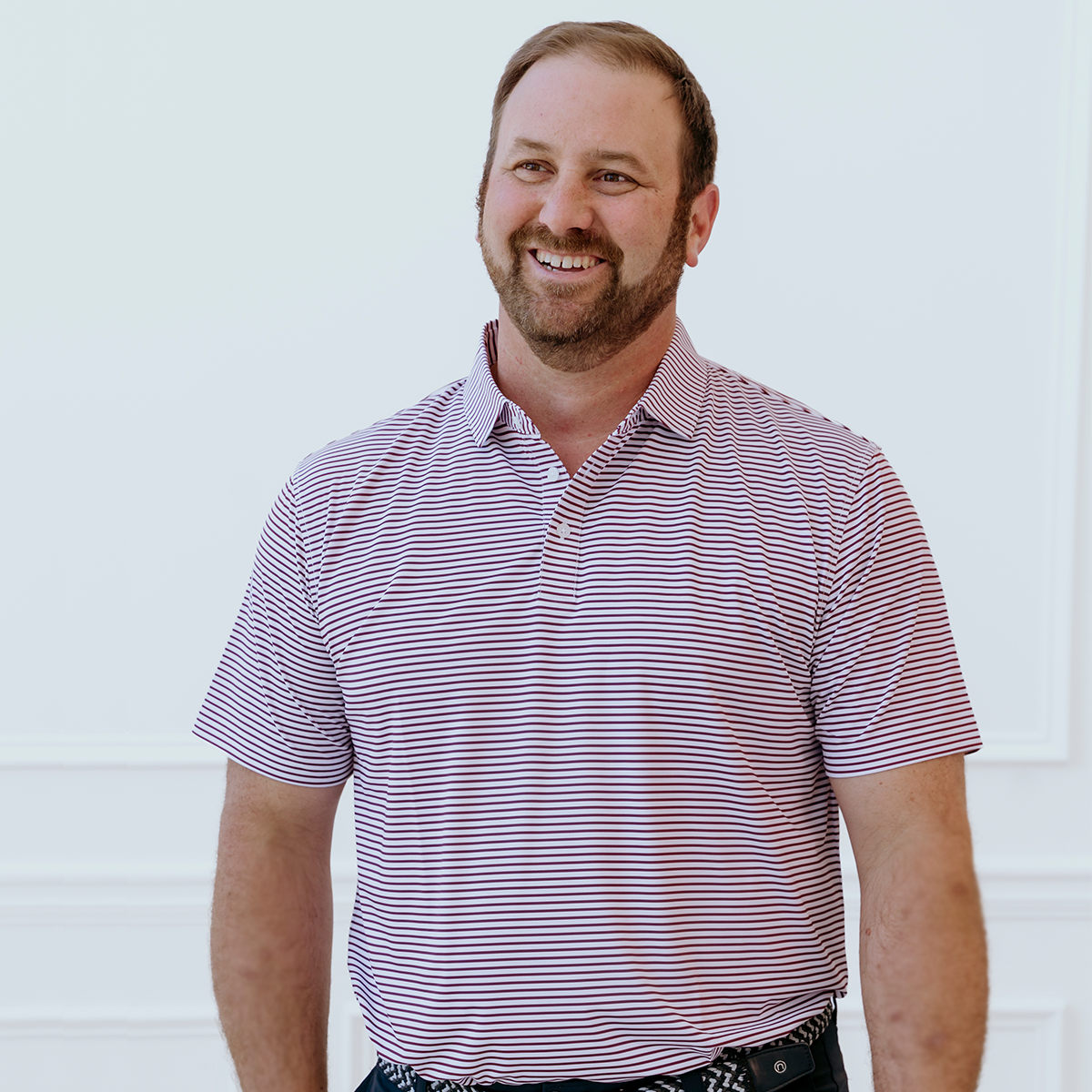 Model wearing the Palmetto Clothing The Classic Stripe Polo in Garnet, one of our high quality golf shirts combining premium comfort, timeless striped style, and exceptional performance on and off the course.