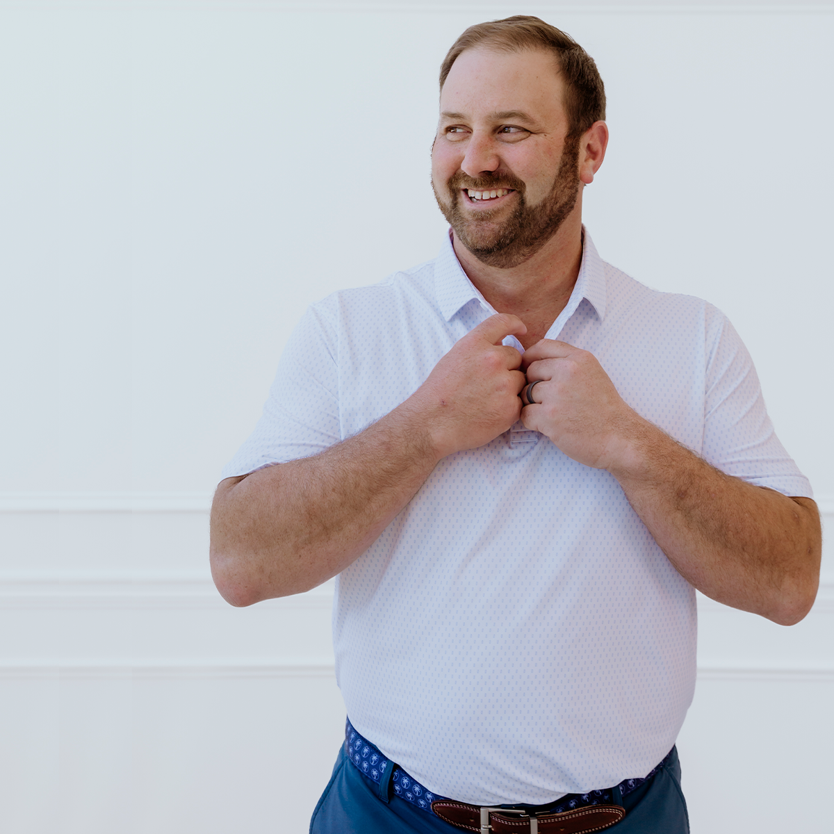 Model wearing the Palmetto Clothing The Flake Polo in White with Blue Flake pattern, a premium patterned golf polo crafted with lightweight performance fabric, exceptional comfort, and timeless style for golfers on and off the course.