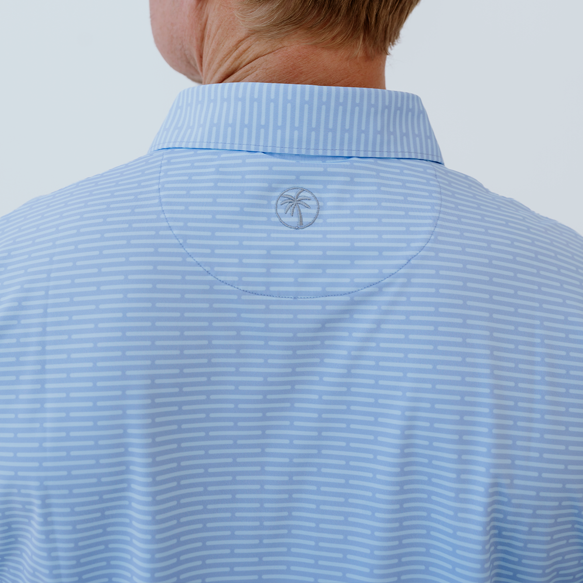 Back view of the Palmetto Clothing The Pin Dash Polo in Medium Blue highlighting the athletic fit, lightweight construction, and breathable performance fabric built for every round and everyday wear.